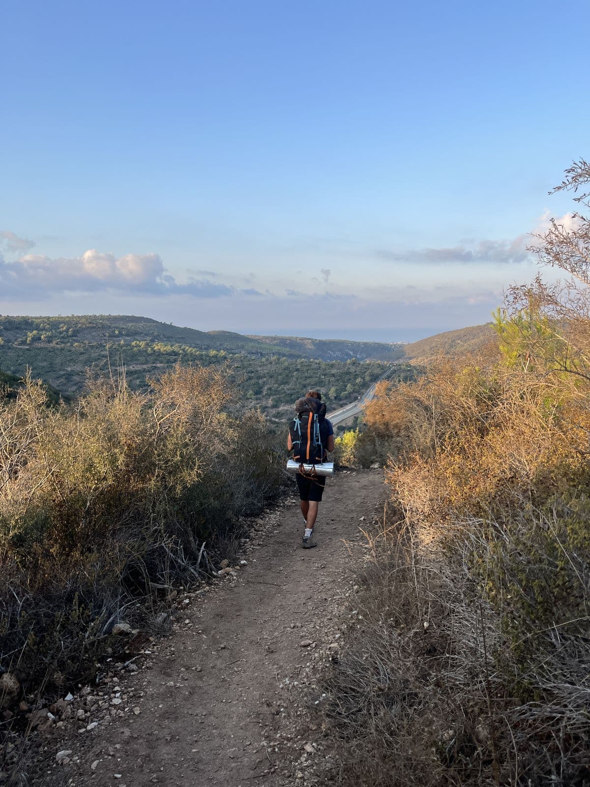 A participant carrying a pack and a mat on a Galilee dirt trail in the last light